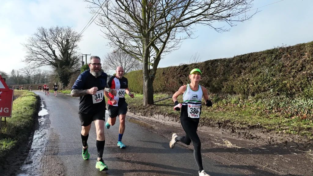 Female runner smiling during a race on country roads with 2 males runners.